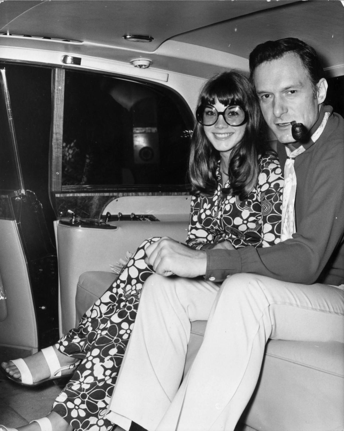 American pornographic magazine publisher and club owner Hugh Hefner with American actress Barbara Benton in a car, leaving London's Hilton Hotel for London airport. Hugh Hefner