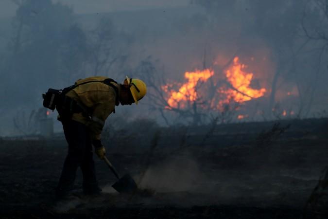 A firefighter works to put out hot spots on a fast moving wind driven wildfire in Orange. California wildfires