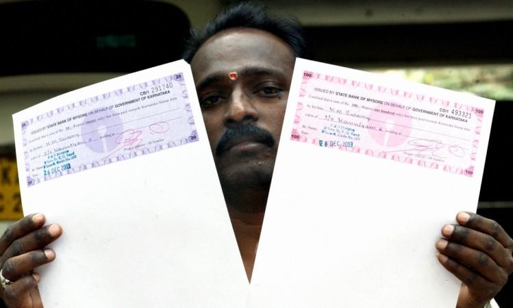In picture: Stamp paper vendor KM Swamy displays the first demand drafts issued from a 'KUBERA' — an automated stamp duty collecting machine after its inauguration in Bangalore, 26 December 2003. Kubera, named after the Hindu God of wealth and money, is the first machine of its kind in the country. The machine's inauguration comes amidst the backdrop of a fraud allegedly masterminded by Abdul Karim Telgi, which is estimated to have cost the state exchequer some Rs 30,000 crore in revenue. Stamp paper is a specially-designed paper produced by the government and used for all legal documents in India ranging from business contracts to divorce papers to rental agreements. Stamp papers