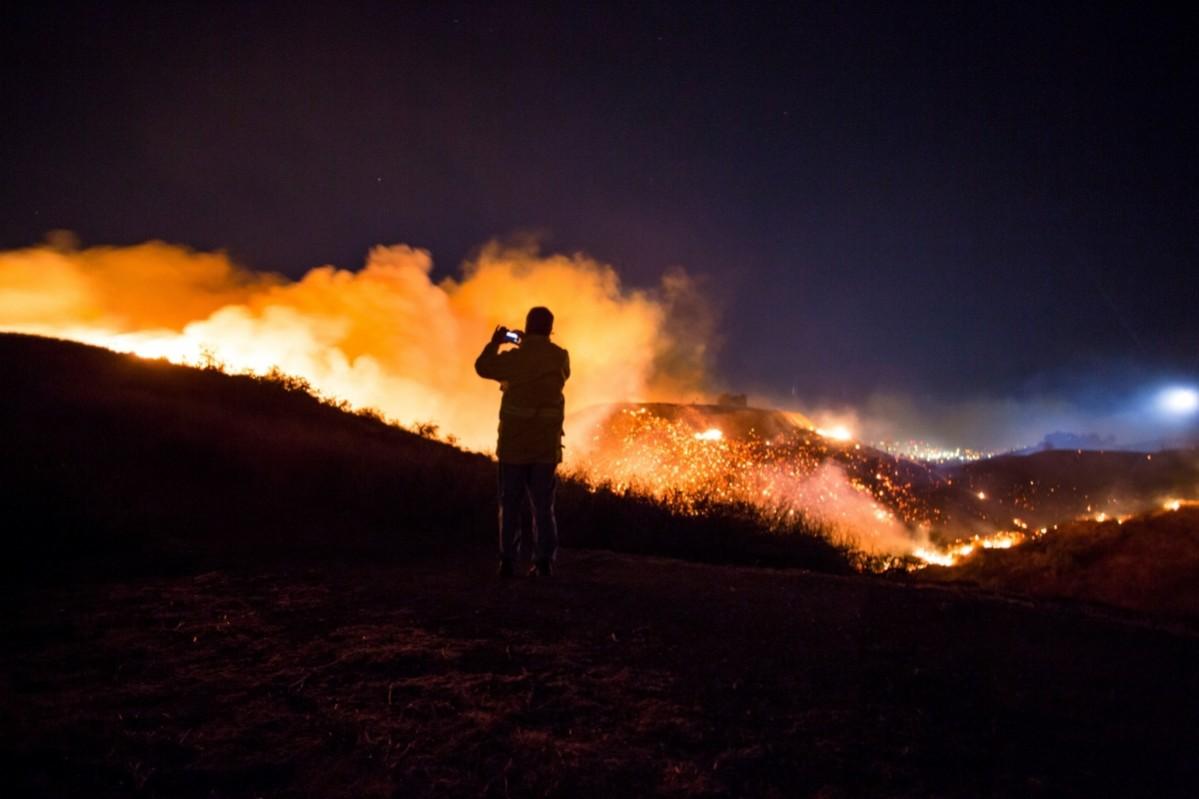 A man watches as the Creek Fire burns along a hillside near homes in the Shadow Hills neighborhood of Los Angeles, California, on December 5, 2017 California wildfire