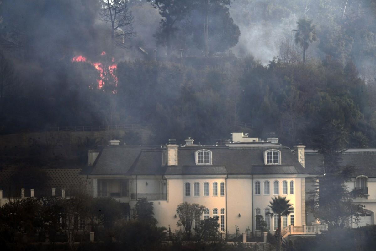 Flames are seen behind a Bel Air mansion threatened by the Skirball Fire in west Los Angeles, California on December 6, 2017 Skirball Fire