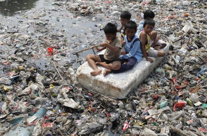 Children sitting on a makeshift raft play in a river full of rubbish in a slum area of Jakarta. Jakarta