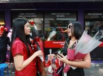 Women chat as they hold flowers during a Valentine's Day celebration in front of a gift shop in Bangkok, Thailand