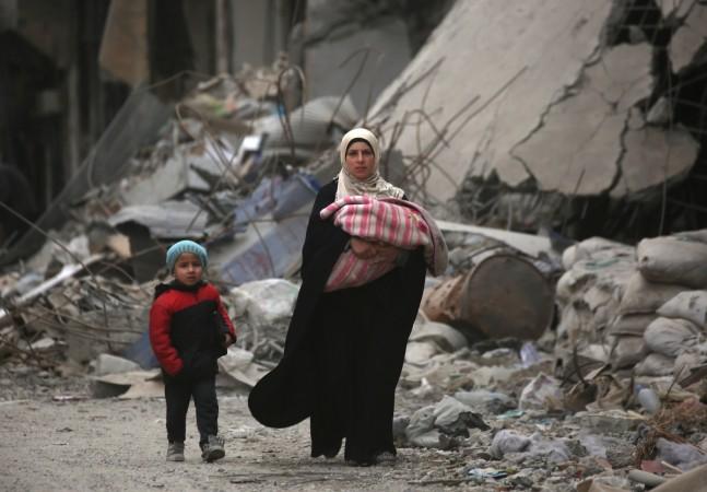 Syrians walk amidst the debris of destroyed buildings in the northern Syrian city of Raqa, on January 11, 2018. ISIS family members
