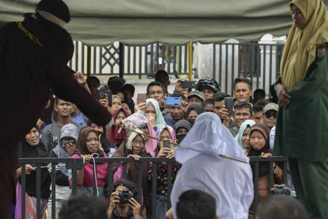 People watch as Tjia Nyuk Hwa, 45, an Indonesian Christian, is publicly flogged outside a mosque in Banda Aceh on February 27, 2018, for playing a children's entertainment game seen as violating Islamic law. Christians flogged in Indonesia