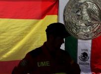 A member of the Spanish Emergency Military Unit (UME) stands in front of the Spanish flag and the Mexican coat of arms and flag,