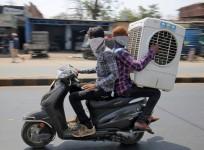 Men transport an air cooler on a two wheeler during a hot summer day