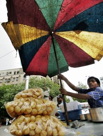 An Indian boy sets up his tattered umbrella to cover his food stall in anticipation of rain at the start of the monsoons in Bombay, 10 June 2004. The boy sells pani-puri, a very popular Indian roadside snack available on almost every street corner. Pani puri