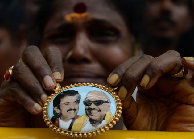 Dravida Munnetra Kazhagam (DMK) party supporter cries as she displays a locket with a portrait of party president M. Karunanidhi (R) in front of the hospital where he is being treated in Chennai on July 30, 2018. - M.Karunanidhi (94) is suffering from a urinary tract infection and is being treated in hospital after sudden variation on blood pressure. karunanidhi