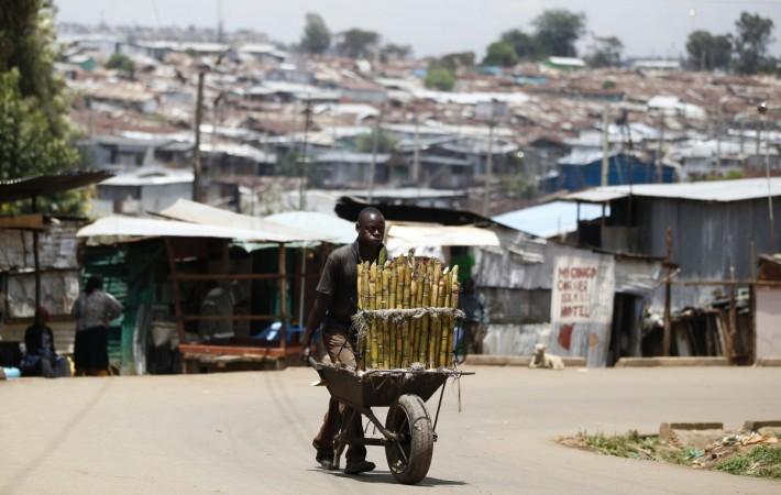 A trader pushes wheelbarrow loaded with sugar-cane for sale along a street in Kibera slum in Kenya sugar cane kenya