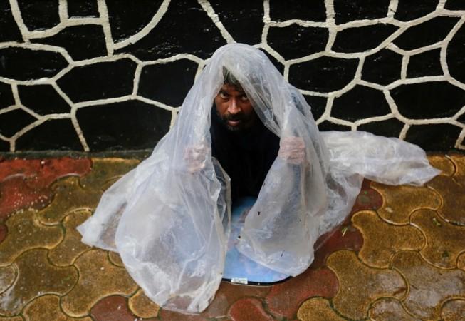 A homeless man takes cover under a plastic sheet as it rains in Mumbai. poverty india