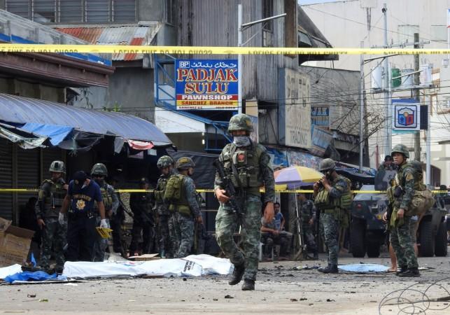 Policemen and soldiers keep watch as body bags (in white), containing the remains of blast victims, as seen in a cordoned area outside a church in Jolo, Sulu province on the southern island of Mindanao, on January 27, 2019. - At least 18 people were killed when two bombs hit a church on a southern Philippine island that is a stronghold of Islamist militants, the military said on January 27, days after voters backed the creation of a new Muslim autonomous region. Policemen and soldiers keep watch as body bags (in white), containing the remains of blast victims, as seen in a cordoned area outside a church in Jolo