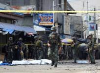 Policemen and soldiers keep watch as body bags (in white), containing the remains of blast victims, as seen in a cordoned area outside a church in Jolo