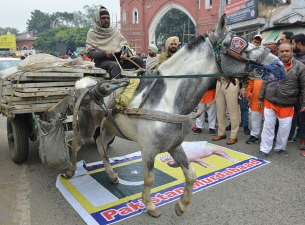 An Indian man on his chariot crosses over a banner depicting a Pakistani flags and an image of Jaish-e-Mohammad group chief, Maulana Masood Azhar, as activists of Hindu Suraksha Samiti (HSS) shout slogans against Pakistan during a protest against the killing of Central Reserve Police Force (CRPF) troopers in Pulwama district in Jammu and Kashmir, in Amritsar on February 17, 2019. INDIA-PAKISTAN-UNREST-KASHMIR