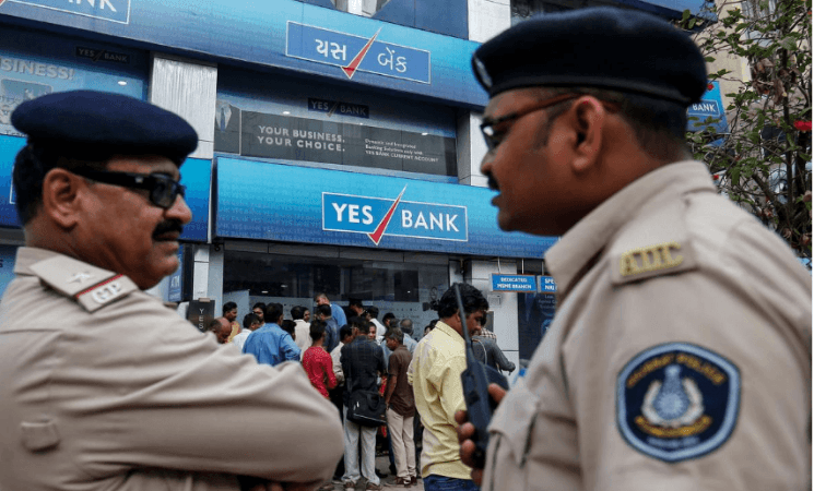 Policemen stand guard as people wait outside a Yes Bank branch to withdraw their money in Ahmedabad, March 6, 2020. yes bank