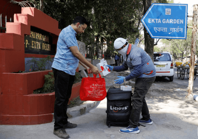 Delivery worker Devender Singh, who works for Licious, an online meat store, passes an order to a customer, during a 21-day nationwide lockdown to slow the spreading of the coronavirus disease (COVID-19), in New Delhi, India, April 6, 2020. devender singh