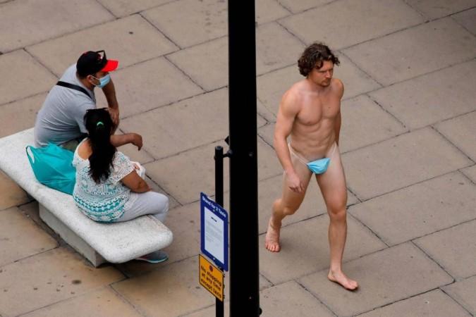 Un hombre con una máscara quirúrgica mientras G-string pasa junto a una mujer, mientras continúa la propagación de la enfermedad por coronavirus (COVID-19), en Oxford Street en Londres, Gran Bretaña, 24 de julio de 2020. REUTERS / Simon Dawson