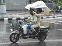 Commuters hold a piece of cloth ride past during rain in Bengaluru on Friday,