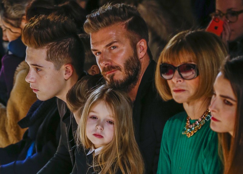 Former England captain David Beckham sits next to U.S. Vogue editor Anna Wintour (2nd R) with his daughter, Harper, on his lap and son Brooklyn (L) Fathers' Day,Fathers' Day 2015,Hollywood celebs with their Kids,celebs with their Kids,Happy Father's Day,dads and their kids,celebrities with their kids,celebrity kids