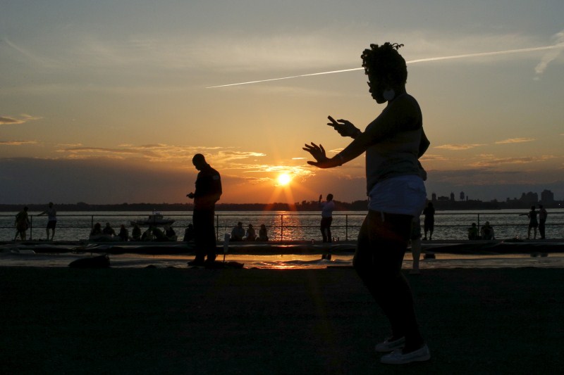 A woman dances as people enjoy a sunny afternoon during the solstice day at Governors Island in New York Couple kiss,Couple kiss during the solstice day at Governors Island,solstice day at Governors Island,Governors Island,solstice day,Couple kisses during the Solstice day at Governors Island
