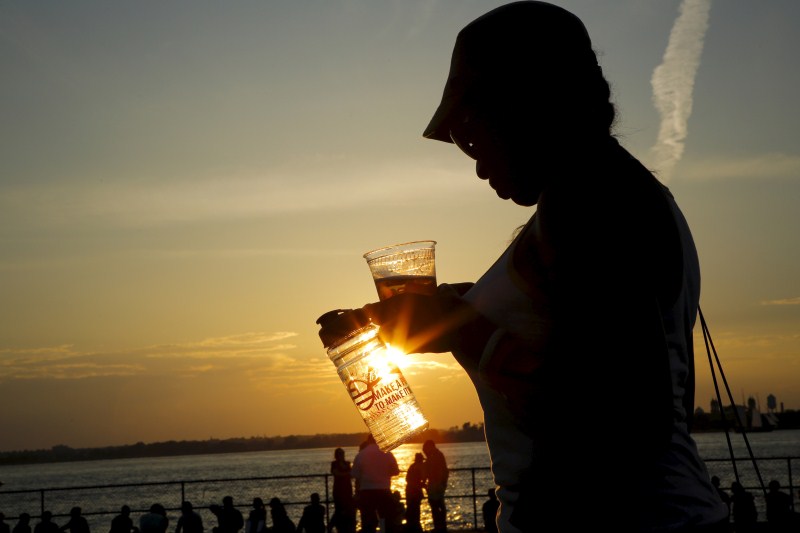 A woman carries some drinks while she enjoys a sunny afternoon during the solstice day at Governors Island in New York Couple kiss,Couple kiss during the solstice day at Governors Island,solstice day at Governors Island,Governors Island,solstice day,Couple kisses during the Solstice day at Governors Island
