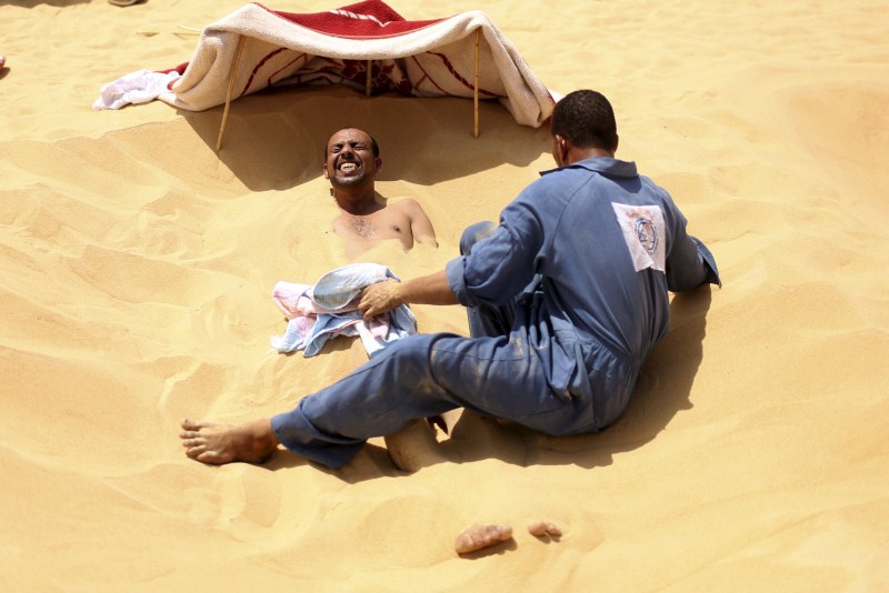 Patients relax in the shade before treatment, which includes massages by the feet of health workers who also submerge their patients up to their neck in the desert. Patients drink mint tea in tents following the treatment. Hot Sand Baths of Siwa,Hot Sand Baths,Patients Sand Baths of Siwa,desert,Patients,treatment,sand bath treatment,sand bath