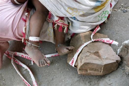 A toddler is tied to a rock in the searing heat, while her parents work at a construction site for $3.80 each a day in India.
