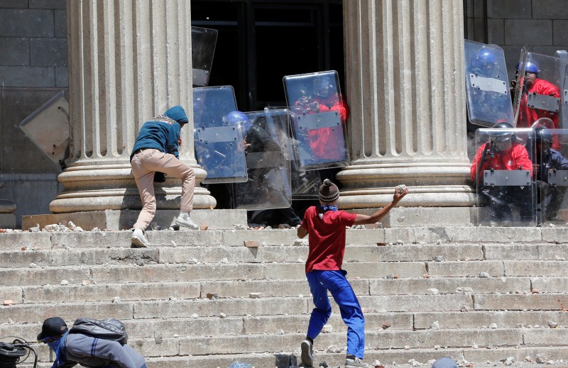 A demonstrator hurls rocks at shield-wielding private security guards during student protests demanding free education at the Johannesburg's University of the Witwatersrand, South Africa. Student protests,Student protests in South Africa,university education,Students demanding free education,Johannesburg University