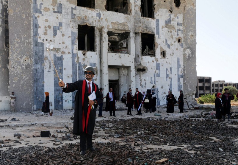 A new graduate of Benghazi University takes a selfie in front of a ruined building at his university's former headquarters. College graduates,Benghazi University,Libyan school,Student clashes,College graduates in a war zone