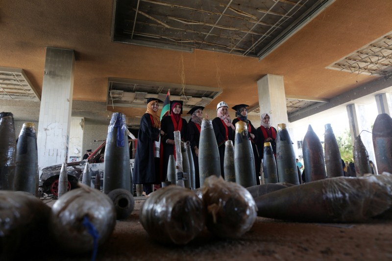 New graduates of Engineering and Law faculties at Benghazi University pose behind disarmed shells at the headquarters of their former university. College graduates,Benghazi University,Libyan school,Student clashes,College graduates in a war zone
