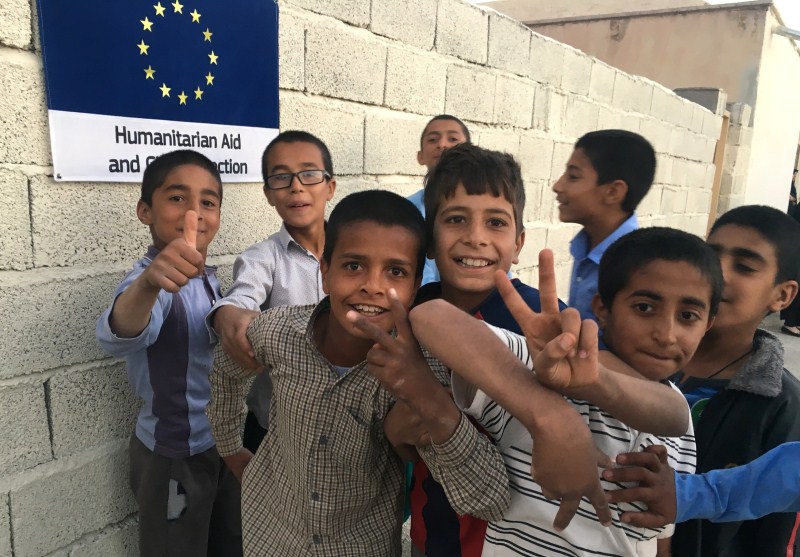 Afghan refugee boys pose next to the EU humanitarian aid sign posted outside their school in the Bardsir settlement for Afghan refugees in Kerman province, Iran. Afghan refugees,Afghan refugees in Iran,Soviet invasion,Taliban insurgency,Islamic State attacks,Islamic attacks,Afghans,Taliban,refugees,refugees in Iran,Islamic refugees attacks
