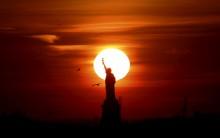 The sun sets behind the Statue of Liberty in New York's Harbor as seen from Brooklyn.