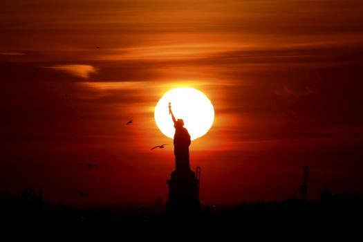 The sun sets behind the Statue of Liberty in New York's Harbor as seen from Brooklyn.