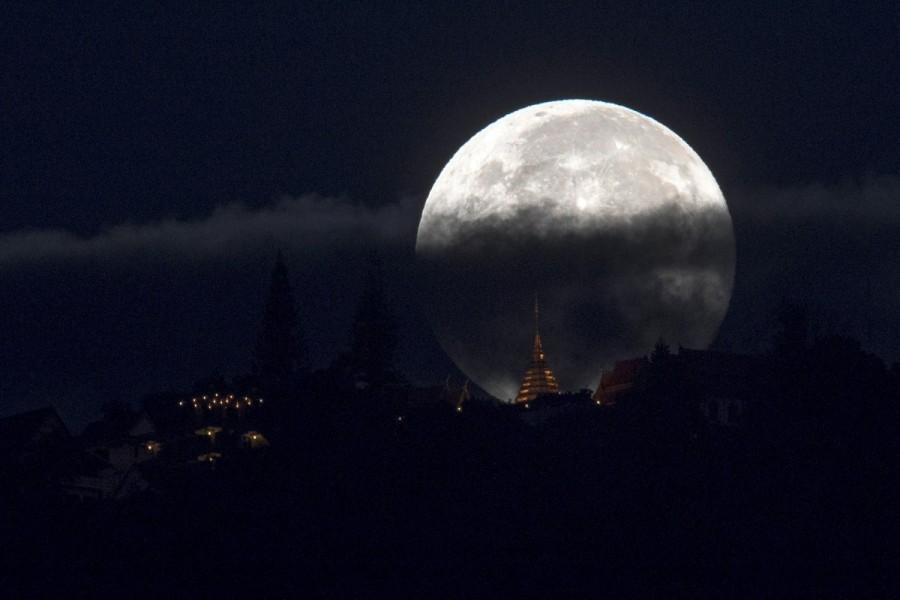 The supermoon is partly covered by clouds as it sets behind Wat Phrathat Doi Suthep in the northern capital of Chiang Mai, Thailand. Supermoon,Supermoon around world,Supermoon in india,Supermoon pics,Supermoon images,Supermoon stills,Supermoon pictures,Supermoon photos,Supermoon new pics