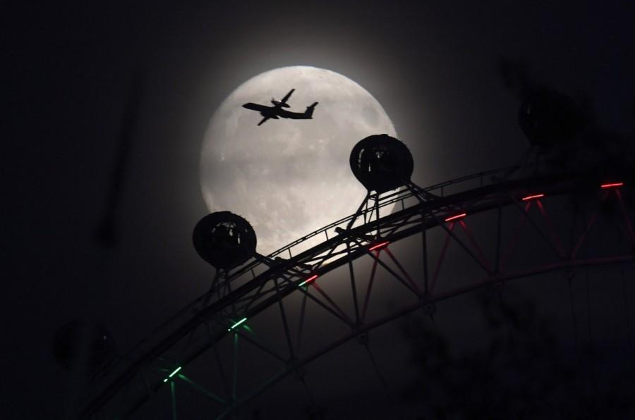 An aeroplane flies past the London Eye wheel, and moon, a day before the "supermoon" spectacle in London, Britain. Supermoon,Supermoon around world,Supermoon in india,Supermoon pics,Supermoon images,Supermoon stills,Supermoon pictures,Supermoon photos,Supermoon new pics
