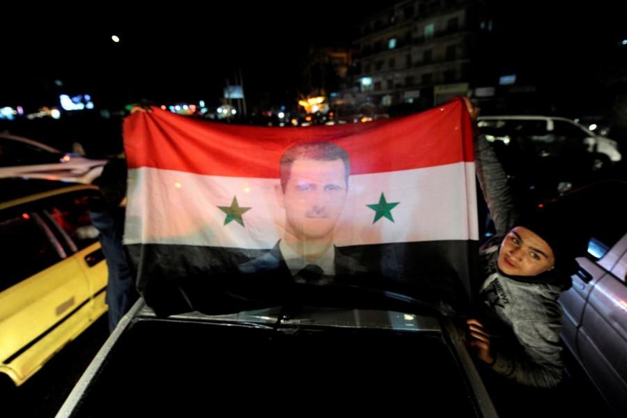 Supporters of Syria's President Bashar al-Assad carry a Syrian national flag with his picture as they celebrate what they say is the Syrian army's victory against the rebels, in Aleppo, Syria December 12, 2016. Aleppo's rebels,Aleppo rebels,Rebels Holding Out in Aleppo Video,Aleppo Video,Beleaguered Rebels,President Bashar al-Assad,Bashar al-Assad