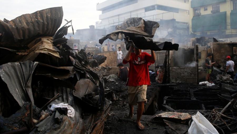 A fire victim collects recyclable materials from the ruins of his house. Philippine slum,Fire at Philippine slum,Manila shantytown