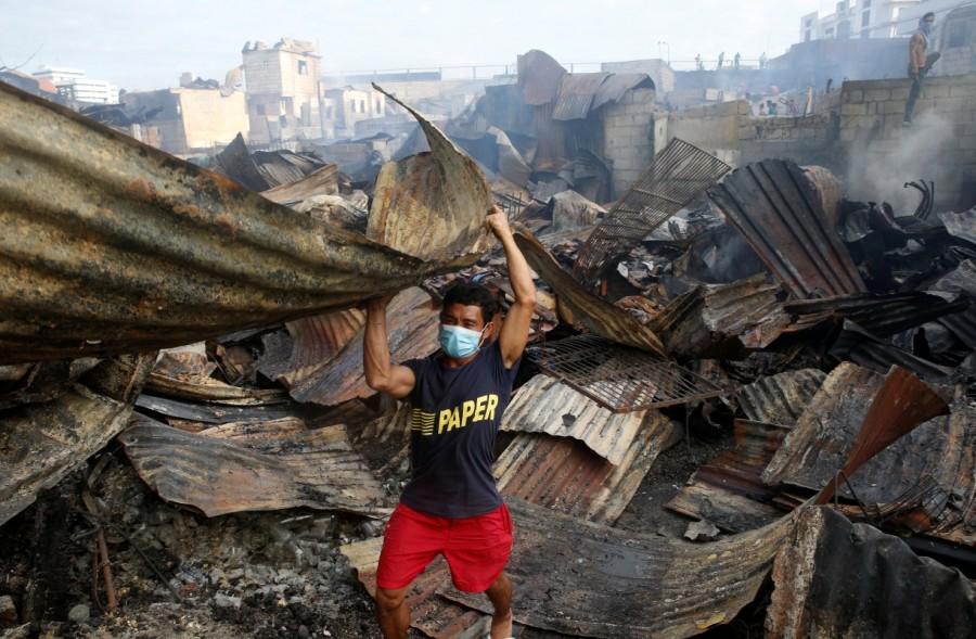 A fire victim carries recyclable materials on his head after the fire. Philippine slum,Fire at Philippine slum,Manila shantytown