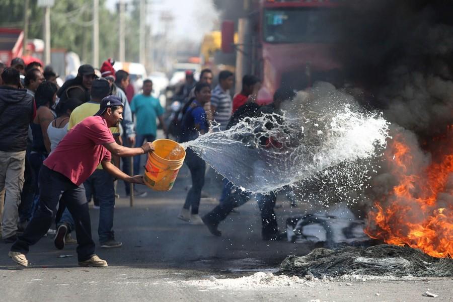 A man throws water on burning tires during a protest against the rising prices of gasoline enforced by the Mexican government at the side of a Pemex gas station in San Miguel Totolcingo, Mexico. Mexicans,Mexico gas price hike,gas price hike,gasoline prices,Latin America,blockaded roads