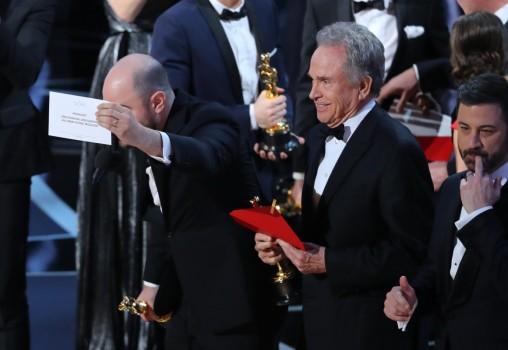 Jordan Horowitz of La La Land holds the card announcing Moonlight as the winner of the Best Picture Oscar as presenter Warren Beatty and show host Jimmy Kimmel stand behind.