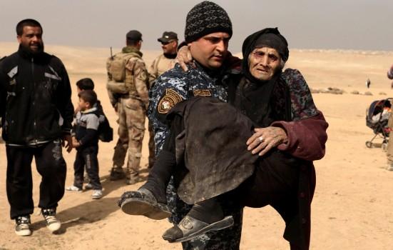 Khatla Ali Abdullah, 90, a displaced Iraqi women who fled her home, is carried by a member of the Iraqi forces in the desert in western Mosul, Iraq.