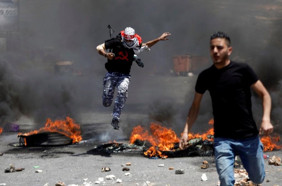 A Palestinian protester jumps over burning tyres during clashes with Israeli troops at a protest marking the 69th anniversary of Nakba, near the Jewish settlement of Beit El, near the West Bank city of Ramallah. Palestinians protest,Palestinians and Israeli forces,Israeli forces,Israel,Israel formation,israel-palestine conflict