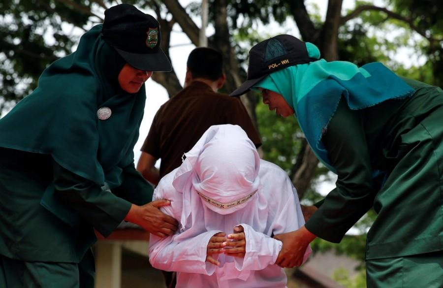 Syariah police women hold an Indonesian woman after being publicly caned for spending time with a man who is not her husband in Banda Aceh, Aceh province, Indonesia. Gay sex,gay sex in Indonesia,Two men publicly caned,Indonesia for having gay sex,Two men caned 83 times for gay sex,Two men caned 83 times