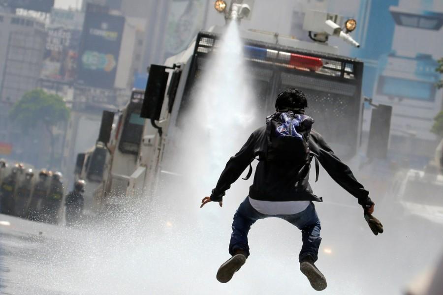 A demonstrator jumps away from a jet of water released from a riot security forces vehicle during a rally against Venezuela's President Nicolas Maduro in Caracas. Venezuela turns water cannons,Venezuela,Venezuela riot police,water cannons,anti-government protesters,protesters
