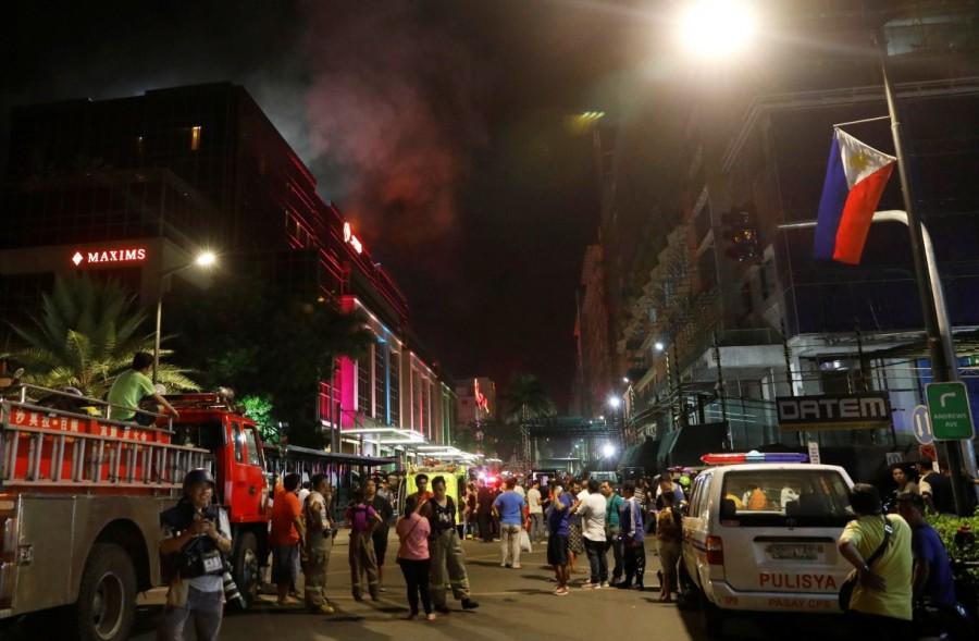 Evacuated employees and guests of hotels stand along a road and watch as smoke billows from a Resorts World building in Pasay City, Metro Manila, Philippines. Gun shots,explosions in Manila,Manila,Explosions in Manila,gunshots in Manila,gunshots at resort,gunshots at resort in Manila