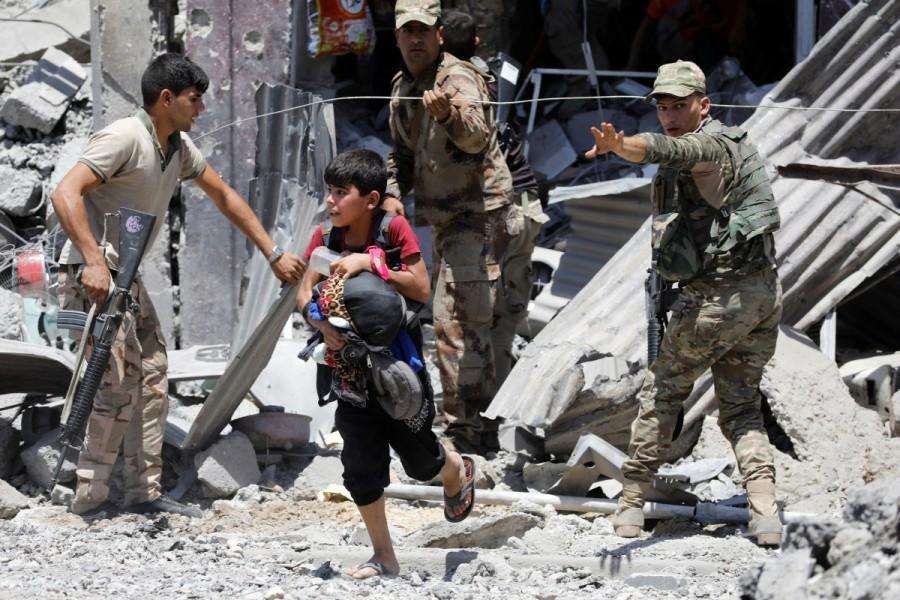A displaced boy who fled his home walks next to Iraqi security forces in al-Zanjili district in western Mosul. Western Mosul,Mosul,Islamic State,Children flee,Islamic State’s last