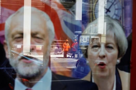 Workers in protective equipment are reflected in the window of a betting shop with a display inviting customers to place bets on tbe result of the general election with images of Britain's Prime Minister Theresa May and opposition Labour Party leader Jeremy Corbyn, in London.