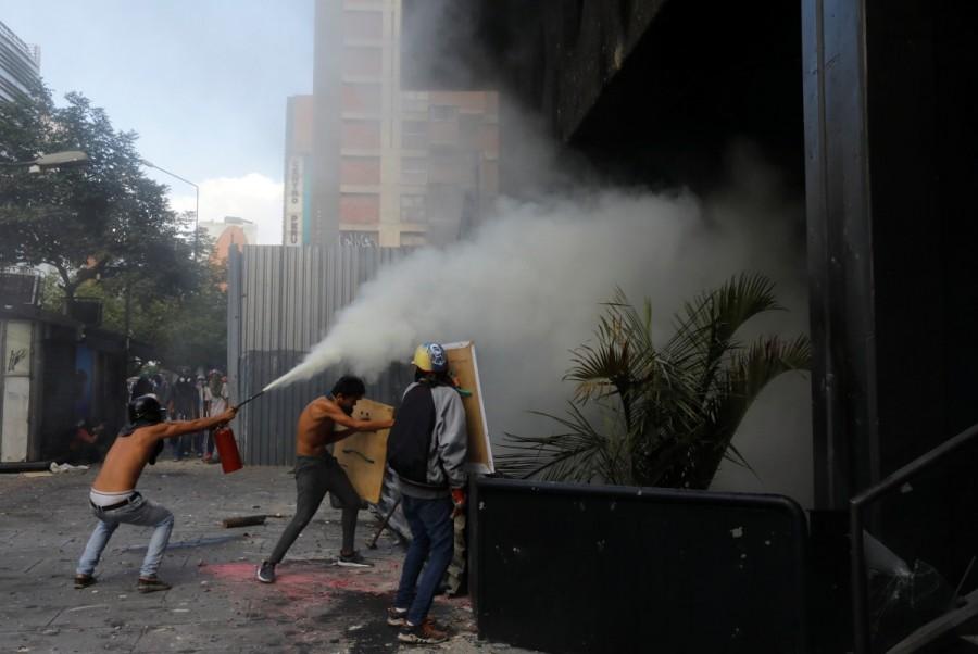 Protesters use a fire extinguisher as a fire burns inside a building housing the magistracy of the Supreme Court of Justice and a bank branch, during a rally against Venezuela's President Nicolas Maduro, in Caracas. Venezuela Supreme Court office,Protesters attack Venezuela Supreme Court office,Protesters angry