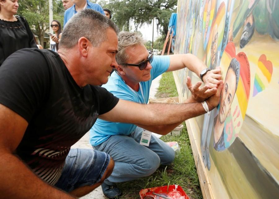 Saul Barrios (L) leaves his handprint on a mural that contains an image of his deceased son Alejandro Barrios Martinez, with the help of artist Yuri Karabash, at the memorial outside the Pulse Nightclub on the one-year anniversary of the shooting in Orlando, Florida. Orlando,Orlando Pulse nightclub massacre,Pulse nightclub massacre,Pulse nightclub,first anniversary of Orlando's Pulse nightclub,Pulse Nightclub,pulse nightclub shooting