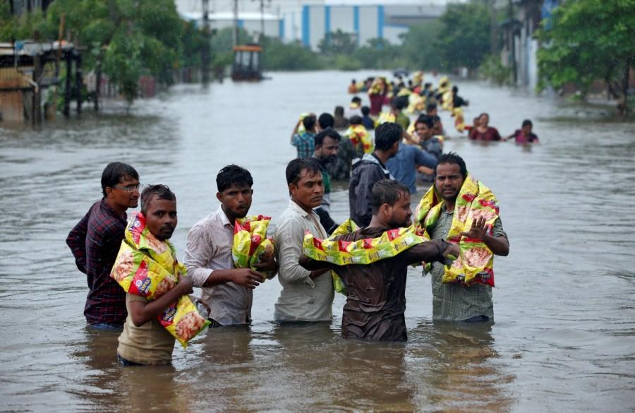 People carry packets of snacks after receiving them from civil defence volunteers in a flooded neighbourhood after heavy rains in Ahmedabad. Deadly monsoon,Deadly monsoon in India,Deadly monsoon rains,Massive floods,Massive floods in India